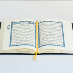 An open Quran on a white table with a yellow bookmark, photographed in a studio setting.