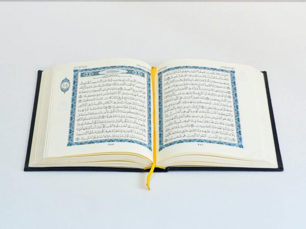 An open Quran on a white table with a yellow bookmark, photographed in a studio setting.